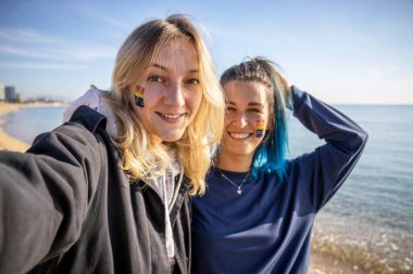 Sahilde selfie çeken iki mutlu LGBT kız arkadaşı. Yüzünde gökkuşağı homoseksüel bayrağı işareti