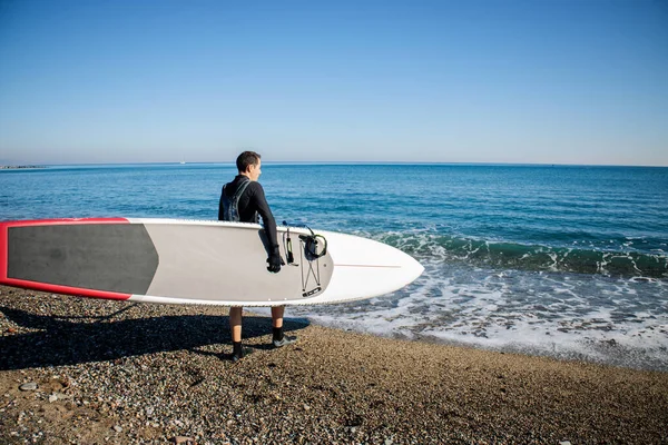 Man with Sup Stand Up Board Going To The Sea. Paddle surf boarding. SUP race board. Active lifestyle water sports concept