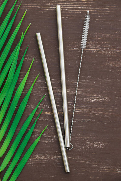 eco-friendly reusable metal drinking straw netx to green leaf on brown woode background. zero waste concept. Vertical picture