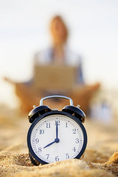 Selective Focus on the clock. Clock on the morning beach, blurred young woman meditating on background. Freelance, time management concept. Stress at Work