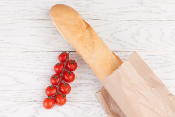 Tomatoes and baguette on a wooden table — Stock Photo, Image