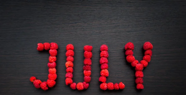 Wort Juli von Himbeeren auf dem Tisch — Stockfoto