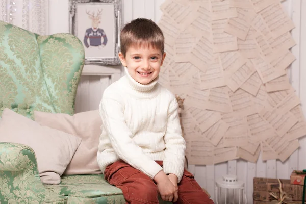 Piccolo ragazzo sorridente sulla sedia in interni di Natale — Foto Stock