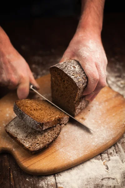 Mannelijke handen snijden vers brood op tafel — Stockfoto