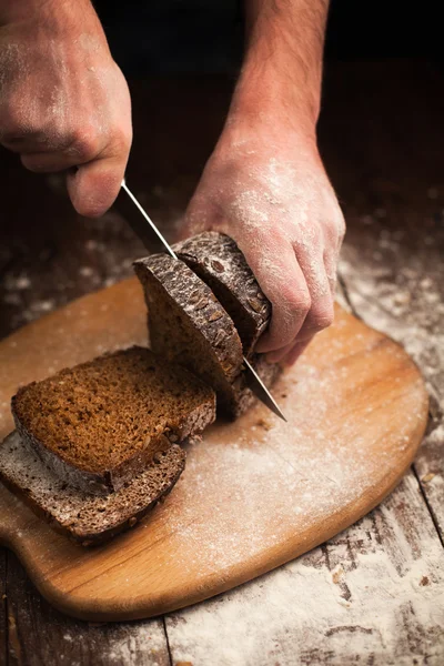 Mannelijke handen snijden vers brood op tafel — Stockfoto