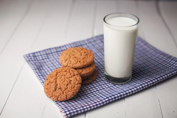 Galletas de avena y vaso de leche en servilleta sobre mesa blanca —  Fotos de Stock