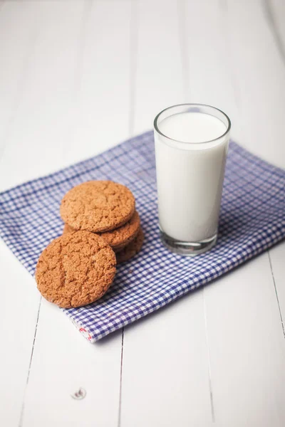 Galletas de avena y vaso de leche en servilleta sobre mesa blanca —  Fotos de Stock