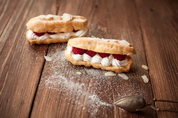 Eclair creme com framboesas frescas na mesa de madeira — Fotografia de Stock