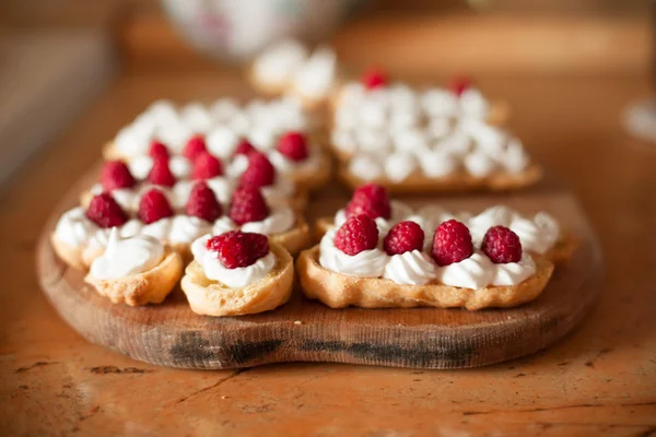 Cream eclairs with fresh raspberries on wood table, cooking — Stock Photo, Image