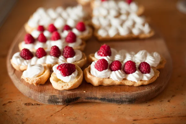 Cream eclairs with fresh raspberries on wood table — Stock Photo, Image