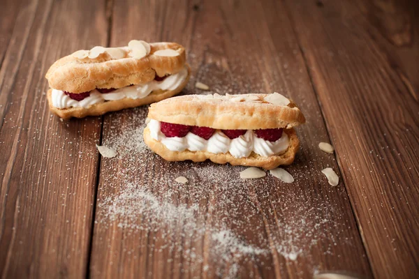 Ahşap masa üzerinde taze ahududu ile krem eklerleri