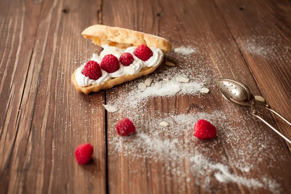 Eclair com framboesas frescas na mesa de madeira, mesa de confeiteiro — Fotografia de Stock