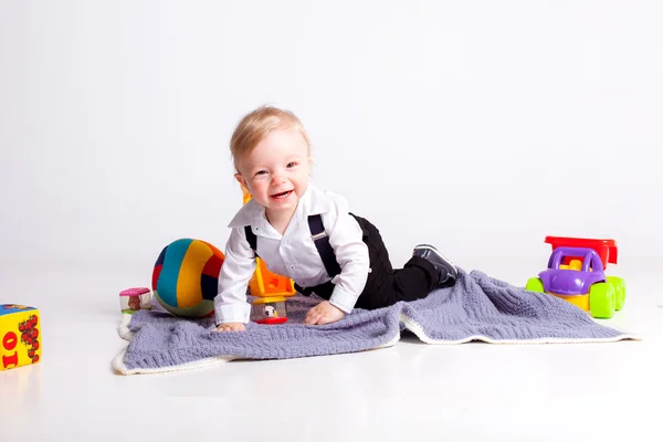 Glimlach jongen zittend op deken met speelgoed op witte achtergrond — Stockfoto