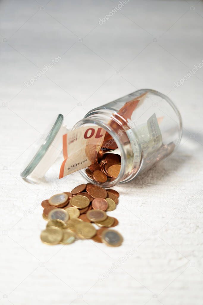 glass piggy bank spilling coins on wooden table. glass jar with euro coins and golden lid. coins scattered around the table. open piggy bank with coins coming out