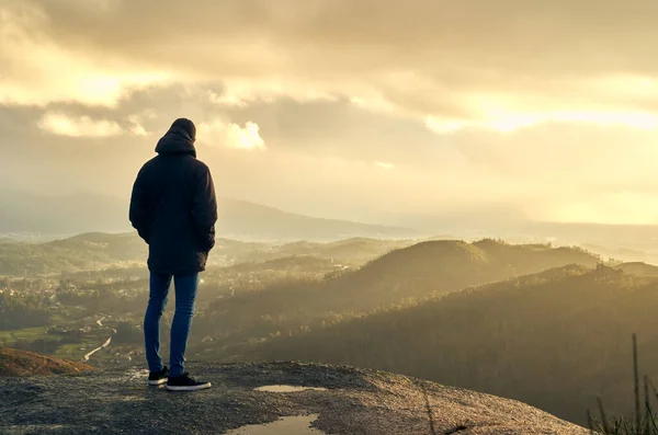 Paltolu, şapkalı ve kot pantolonlu genç bir adam dağın tepesinde güneşin doğuşunu seyrediyor. Gençler kışın gün batımında bir dağın tepesinde düşünür. Galiçya 'nın yeşil ve kayalık dağları.