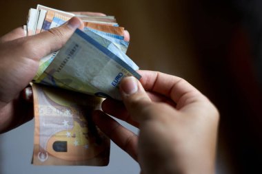 Adamın elleri cüzdanı açıyor ve banknotları çıkarıyor. kişi 50, 20 ve 10 avroluk euro banknotlarını sayıyor. Kahverengi elleri ve kahverengi deri cüzdanı olan renkli cıvatalar.