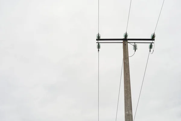 Arka planda bulutlu gökyüzü ve yüksek voltaj kabloları olan elektrik kulesi metalik elektrik kabloları olan gri taş kule..