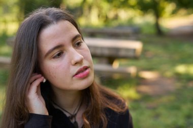 Uzun saçlı, açık tenli kadın doğada beyaz kablosuz kulaklık takıyor. Bluetooth ses cihazları kullanan genç, yeşil bulanık arkaplan. Kız parkta müzik dinliyor.