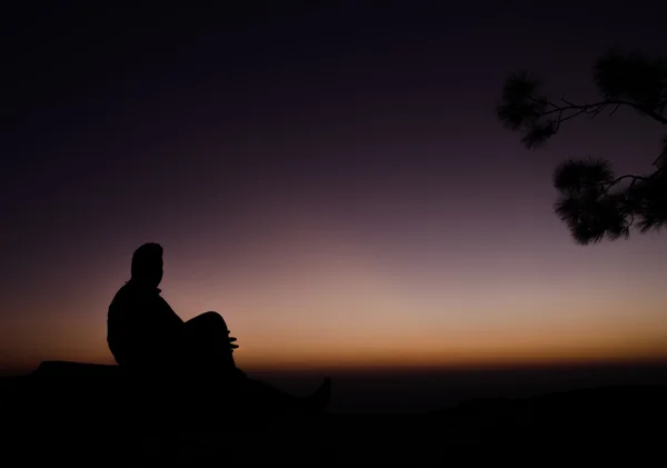 Shadow of man sitting on rock in silhouette with color background — Stock Photo, Image