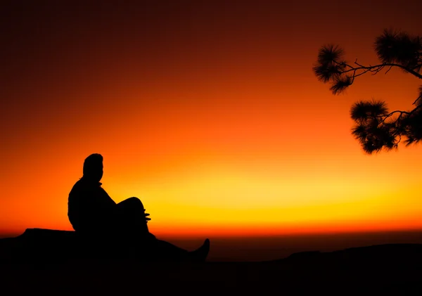 Schatten des Mannes sitzt auf Felsen in Silhouette mit farbigem Hintergrund — Stockfoto