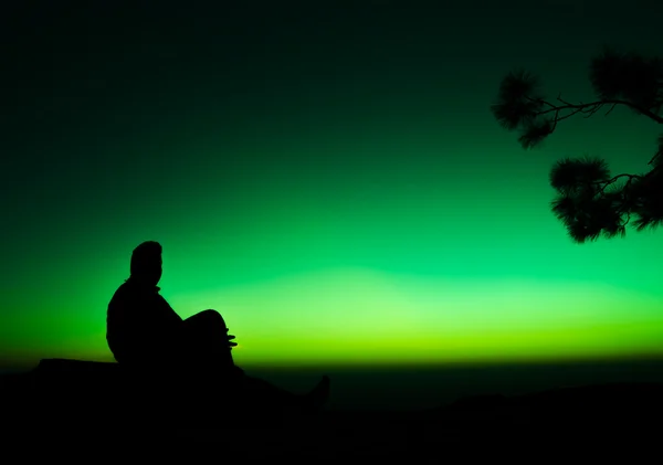 Schatten des Mannes sitzt auf Felsen in Silhouette mit farbigem Hintergrund — Stockfoto