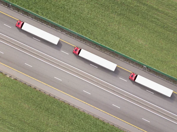 Dumpwagens die goederen vervoeren op de snelweg. Rode vrachtwagen rijden op asfaltweg langs de groene velden. gezien vanuit de lucht. Luchtfoto landschap. drone fotografie. vracht levering Stockfoto