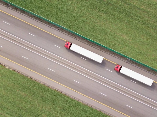 Dumpwagens die goederen vervoeren op de snelweg. Rode vrachtwagen rijden op asfaltweg langs de groene velden. gezien vanuit de lucht. Luchtfoto landschap. drone fotografie. vracht levering Stockfoto