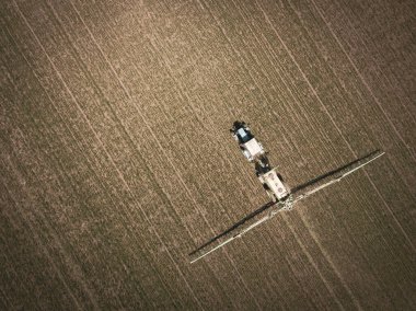 İlkbaharda tarlada, traktörün toprak ve genç mahsulleri püskürttüğü havadan aşağıya doğru bir görüntü. Azov. Rusya.