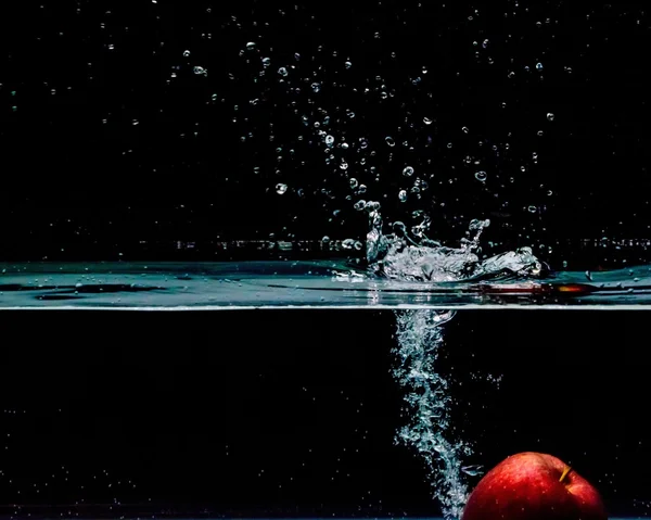 Red apple splashing into water, isolated on black background