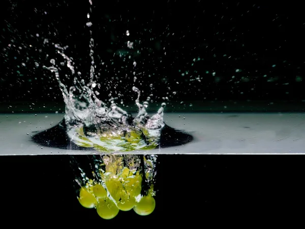 Grüne Trauben ins Wasser, isoliert auf schwarzem Hintergrund — Stockfoto