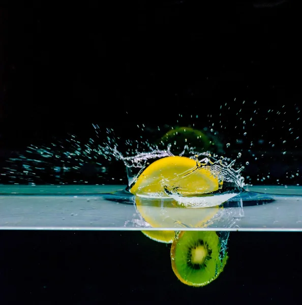 Лимон и киви фрукты в воду, изолированные на черном фоне — стоковое фото