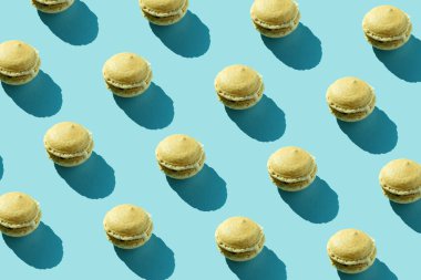 Pastel mavi arka planda renkli Fransız kurabiyeleri deseni. Minimum konsept. Çikolatalı tatlı, renkli yüzeyde badem kurabiyesi. Üst görünüm düzlüğü