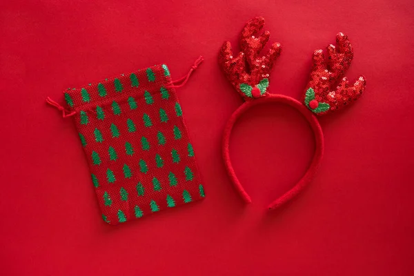 圣诞饰物，鹿角头带上的红色闪光表面和礼品袋，贺卡。最小寒假的想法。平面放置顶部视图 — 图库照片
