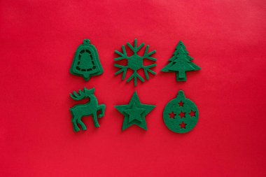 Kraft yeşil oyuncak kompozisyonu hissetti. Kırmızı yüzeyde Noel süslemeleri. Dekor, geyik, kar tanesi, takı, ağaç, yıldız. Üst manzara, düz uzanma