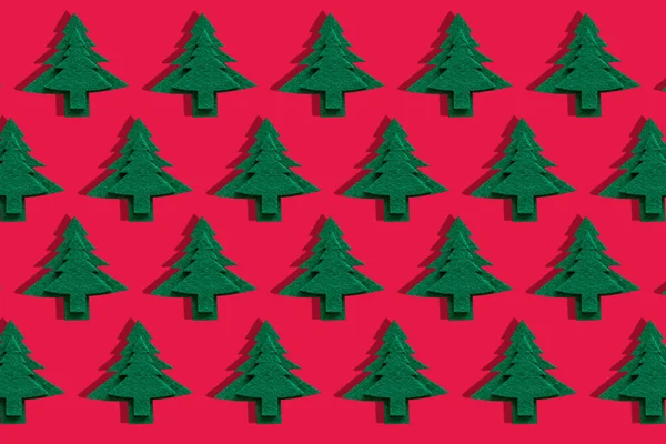 Christmas decorative trees on red surface. Object pattern of holiday felt tree with shadow. Trendy christmas wallpaper. Happy Holiday greeting card, banner.