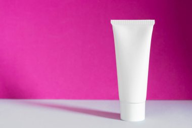 Mor arka planda beyaz krem tüplü boş şişe ambalajı. Güzellik ürünü maket paketi, reklam markası, doğal kozmetik, serum, cilt bakımı. Cilt bakımı nemlendirici kozmetik. Boşluğu kopyala