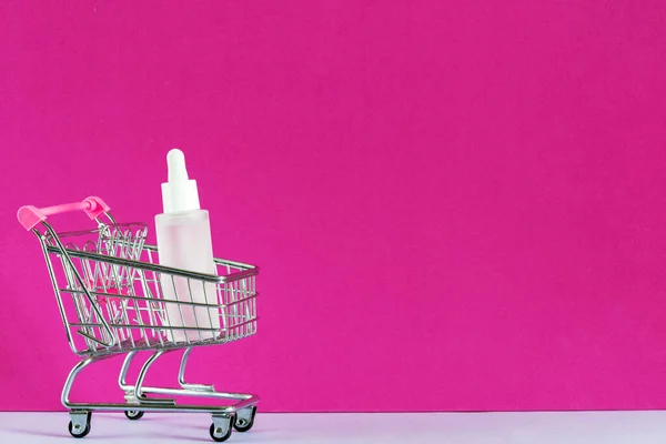 Cosméticos compras on-line conceito de e-commerce. Garrafa de soro, ácido hialurônico para cuidados com a pele no carrinho de compras. Skincare produto de beleza mockup. Loja de cosméticos online. Espaço de cópia, banner — Fotografia de Stock