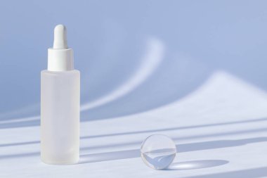 Kolajenle yaşlanma önleyici serum ve gölgeli mavi yüzeyde peptid. Hyaluronik asit yağ modeli. Güneş ışığı ve serum kozmetiğinin gölgesi. Cam şişede şeffaf sıvı ürün