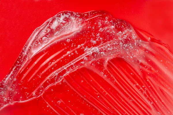 Gel cosmetico sbavatura con bolla. Prodotto trasparente per la cura della pelle su rosso. Un goccio di lozione liquida. Gel sierico. Spalma di acido ialuronico. Campione di lubrificante. Idratante con vitamina. Texture gelatina.. — Foto Stock