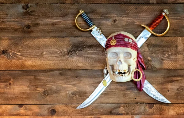Jolly pirate scull in bandanna with crossed swords and golden teeth on wooden background.