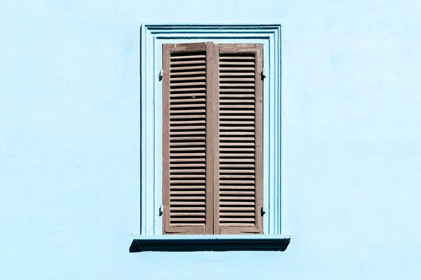 Szare okiennice na oknie pod niebieską ścianą. Stare zewnętrzne w włoskiej lub greckiej wiosce z zamkniętym oknem. — Zdjęcie stockowe