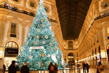 Milan, İtalya - 15 Aralık 2020: Dijital Noel Ağacı Swarovski 2020 Galleria Vittorio Emanuele II 'nin merkezinde Swarovski butiğinin önünde. Covid sırasında maskeli insanlar yürür.