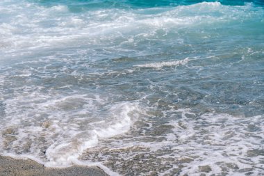 Kumsalda beyaz köpüklü dalgalar var. Deniz kenarında güneşli bir yaz günü.