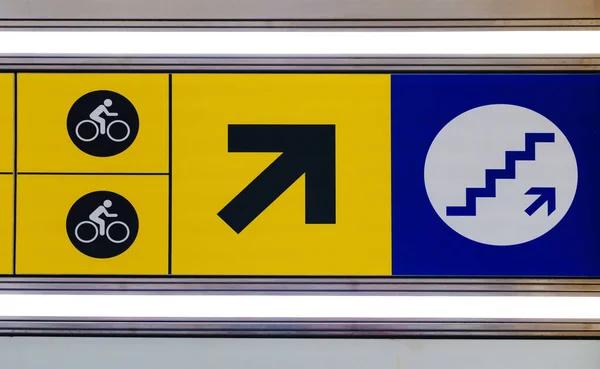 Closeup illuminated direction or information sign upstairs from underground for bicyclists for exit to railway train station platform. — Stock Photo, Image