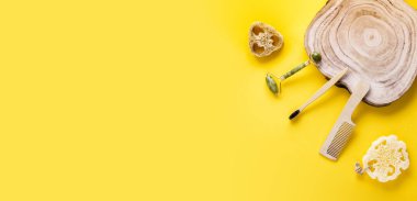 Eko güzellik konsepti. Yeşim yüz silindiri, lif süngeri, diş fırçası, ahşap tarak, sarı yüzeyde ahşap dilimler..