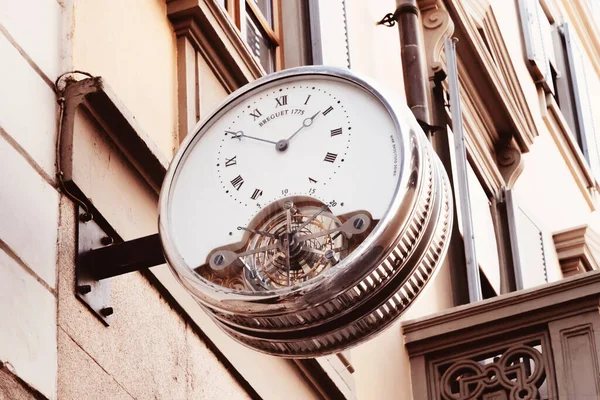 Vintage street clock with roman numerals hanging on the wall of building in center of european city. Outdoor analog sidewalk clocks