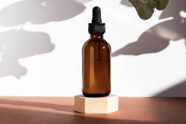 Tahta geometrik kaide podyumunda kehribar kozmetik şişesi bitkilerin doğal gölgeleriyle ürün ambalajı peptitli yaşlanma önleyici serum kozmetik modelleme, cilt konsepti..