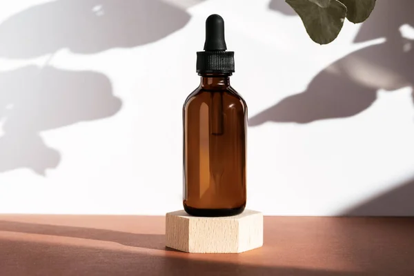 Tahta geometrik kaide podyumunda kehribar kozmetik şişesi bitkilerin doğal gölgeleriyle ürün ambalajı peptitli yaşlanma önleyici serum kozmetik modelleme, cilt konsepti..