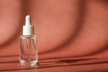 Serum kozmetik şişesi, kahverengi arka planda hyaluronik asit. Peptit, kolajen ve modern cam kozmetik ambalajlı serum ürünü. Kozmetik vitrini