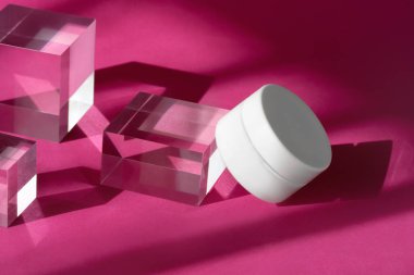 Vücut kremi boş kozmetik gölgeleri ve yansıması olan şeffaf katı bloklarla makara yapıyor. Cam küp kürsünün üstünde duran bir kavanoz organik losyon..